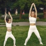 Mother and daughter in matching activewear doing exercises outdoors on a sunny day.